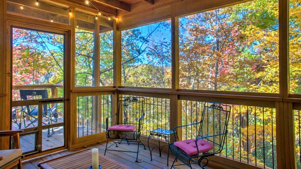 A wooden deck with metal chairs and a table, overlooking a forest with autumn foliage.