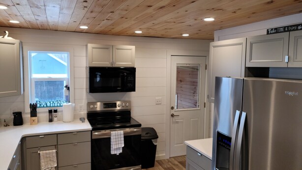 A modern kitchen with stainless steel appliances, wooden ceiling, and white cabinetry.