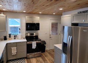 A modern kitchen with stainless steel appliances, wooden ceiling, and white cabinetry.