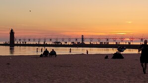 A beach with a pier extending into the water, people sitting and walking along the shore.