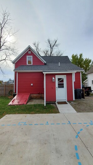 A red single-story house with a white door, a small porch, and a garage door.