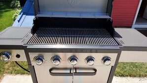A stainless steel outdoor grill with four burners and a digital display, positioned on a concrete patio.