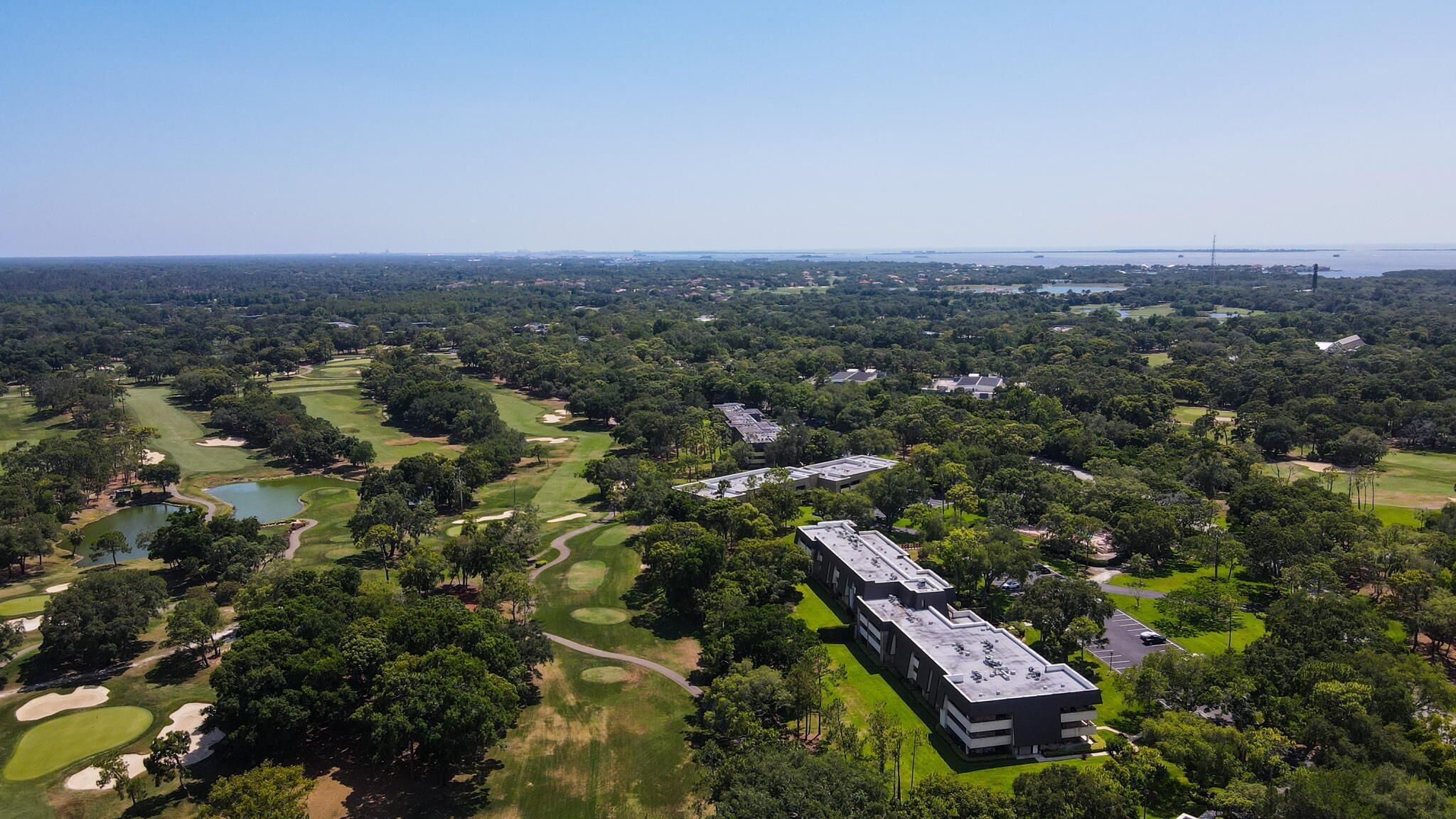 An aerial view of a golf course with a large building complex in the foreground.