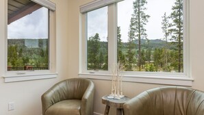 A room with two leather chairs, a small wooden table with decorative items, and large windows offering a view of a forested area.