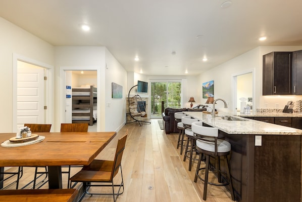 Cozinha moderna com ilha central, área de refeições com mesas de madeira e vista para o exterior.