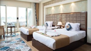 A hotel room with two beds, a balcony, a desk, and a view of the city. - Nile Transport Hotel (Shubra al Khaymah)