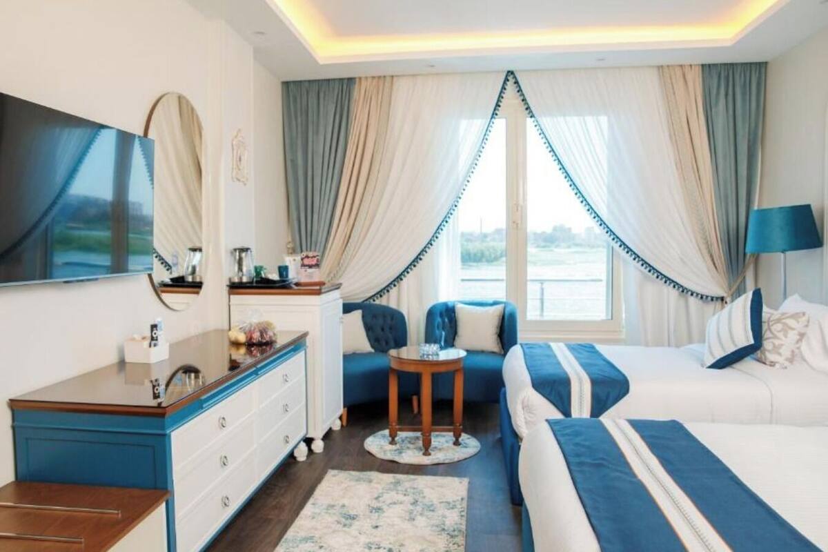 A hotel room with a bed, a sofa, a desk, a TV, and a view of the outdoors.