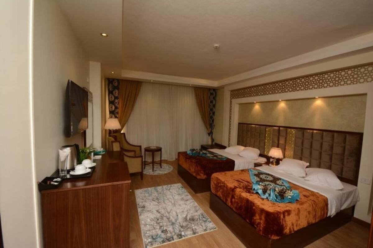 A hotel room with two beds, a desk, a chair, a TV, and a decorative headboard.