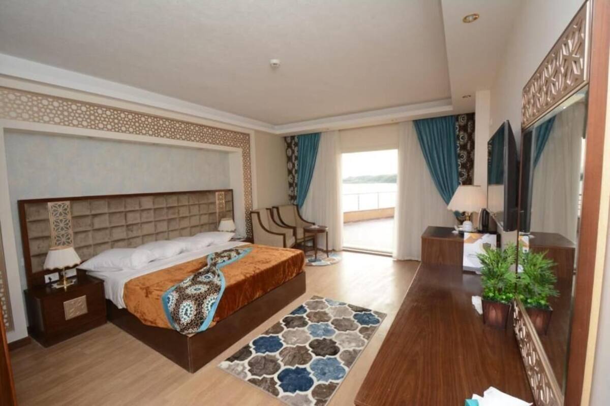 A hotel room with a bed, bedside table, TV, and a view of the outdoors.