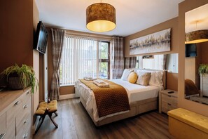 A modern hotel room with a large bed, a bedside table, a TV, and a window with curtains. - Peaceful + Charming 2 BR Home in Rathmines, Dublin (Dublin 6)