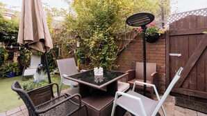 An outdoor patio with a table and chairs, surrounded by a garden and a wooden fence.