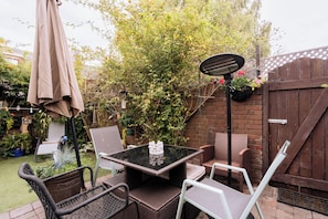 An outdoor patio with a table and chairs, surrounded by a garden and a wooden fence.