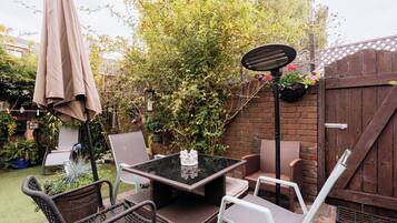 An outdoor patio with a table and chairs, surrounded by a garden and a wooden fence.
