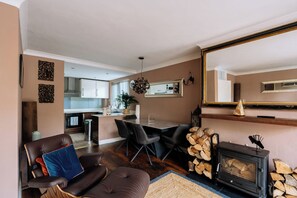 Un salon moderne avec une cheminée, un coin repas et une cuisine visible à travers une porte ouverte.