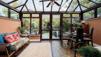 A conservatory with a glass ceiling, wooden furniture, and a variety of plants.
