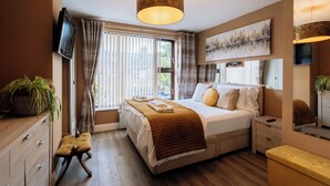 A modern bedroom with a large bed, bedside tables, a TV, and a window with curtains.
