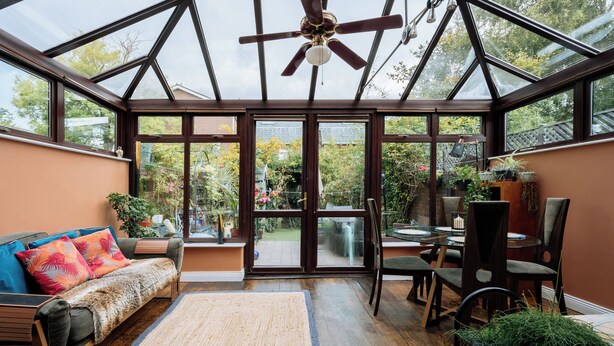 A conservatory with a glass ceiling, wooden furniture, and a variety of plants.