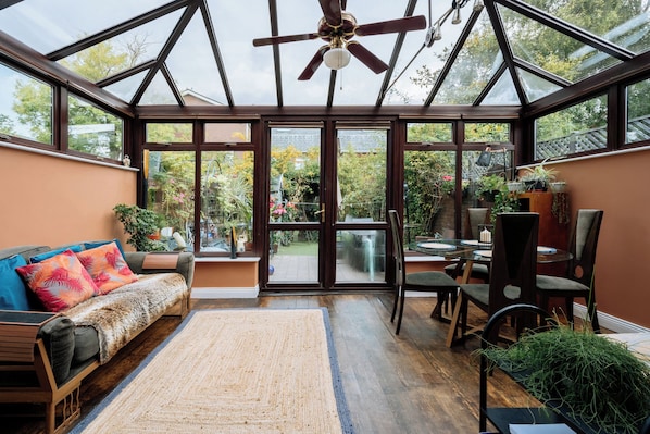 A conservatory with a glass ceiling, wooden furniture, and a variety of plants.