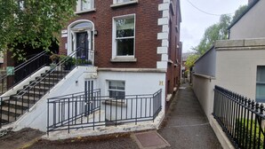 A narrow street with a staircase leading to a building with a white and red facade.