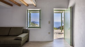 A room with a sofa, two windows with green frames, and a view of the sea.