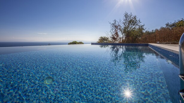 A clear blue infinity pool with a view of the ocean and a clear sky.