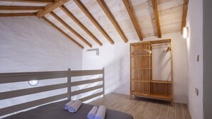 A bedroom with a wooden ceiling, a bed with a dark bedspread, and a wooden wardrobe with a hanging rack.