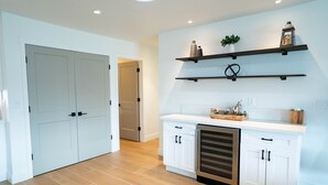 A kitchen with white cabinets, a dishwasher, and wooden flooring. There are two shelves above the counter with decorative items. - ✻ Scottsdale ✻ OASIS W/ POOL & GOLF, 4 Bed 2 Bath (Scottsdale)