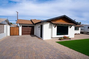 Enter through a wooden gate to a single-story house with a brick facade and sloped roof.