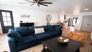 A modern living room with a dark blue sectional sofa, a coffee table with a bowl of snacks, and a brown leather ottoman. - ✻ Scottsdale ✻ OASIS W/ POOL & GOLF, 4 Bed 2 Bath (Scottsdale)