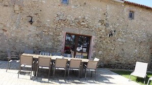 Un área de comedor al aire libre con un muro de piedra, una mesa con sillas y una ventana pequeña.