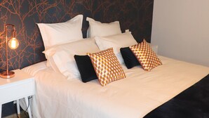 Un dormitorio con cama, ropa de cama blanca, una manta negra y una mesita de noche con lámpara.