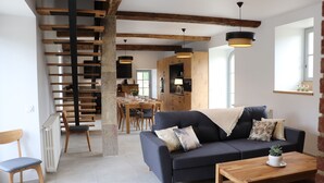 Una sala moderna con un sofá oscuro, una mesa de comedor de madera y una escalera con vigas a la vista.