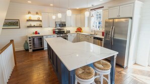 Une cuisine moderne avec des meubles blancs, un grand îlot central, des appareils en acier inoxydable et des luminaires suspendus.