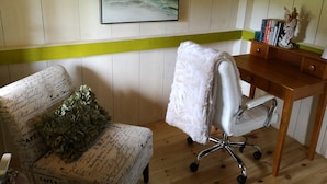 Una habitación con un escritorio de madera, una silla blanca con cubierta mullida, una pared de acento verde y un cuadro abstracto enmarcado.