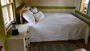 Un dormitorio con cama, almohadas, una mesita de noche y una ventana.