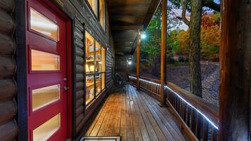 A wooden cabin with a red door, a covered porch, and a view of trees.