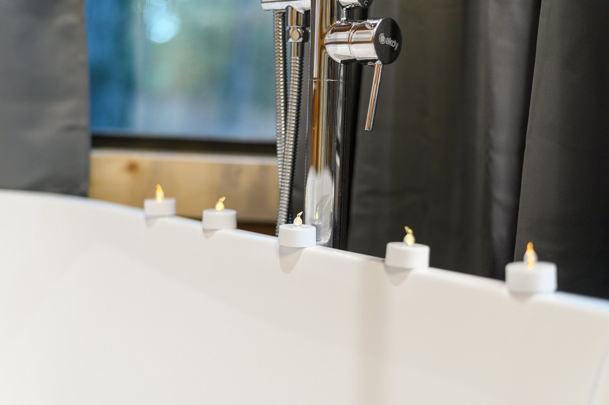 A modern bathroom with a bathtub, a shower, and a mirror. There are candles placed on the edge of the bathtub.