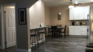 Una cocina compacta con armarios blancos, una zona de comedor con mesa y sillas, y un ventilador de techo.