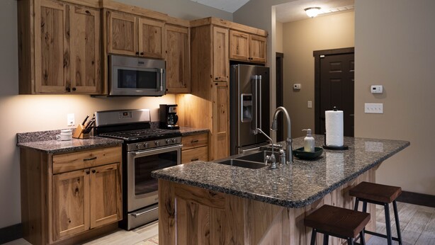 Una cocina con armarios de madera, electrodomésticos de acero inoxidable, encimeras de granito y un taburete de bar.