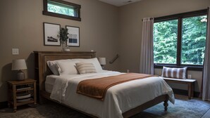 Un dormitorio con una cama grande, mesitas de noche, una ventana con vista a árboles y cuadros en la pared.