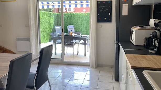 A modern kitchen with a sliding glass door leading to an outdoor dining area, a refrigerator, and a microwave. - Superbe Pavillon Tout Confort Proche de la mer (Narbonne)