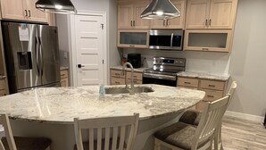 A kitchen with a central island, stainless steel appliances, wooden cabinets, and a marble countertop. - Direct Lakeside View, 5 bed, 2.5 bath Condo at Bridges Bay (Arnolds Park)