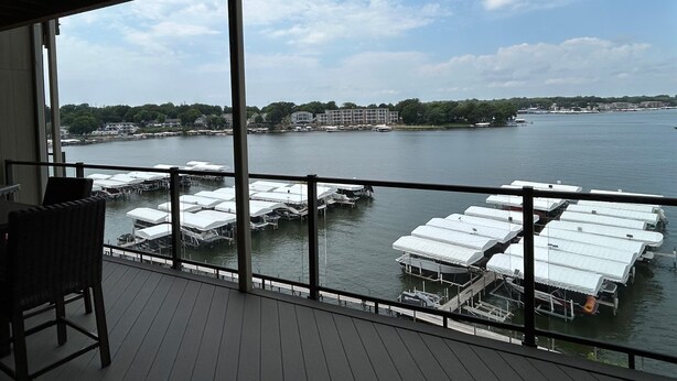 A balcony with a view of a marina, docked boats, and buildings across the water. - Direct Lakeside View, 5 bed, 2.5 bath Condo at Bridges Bay (Arnolds Park)
