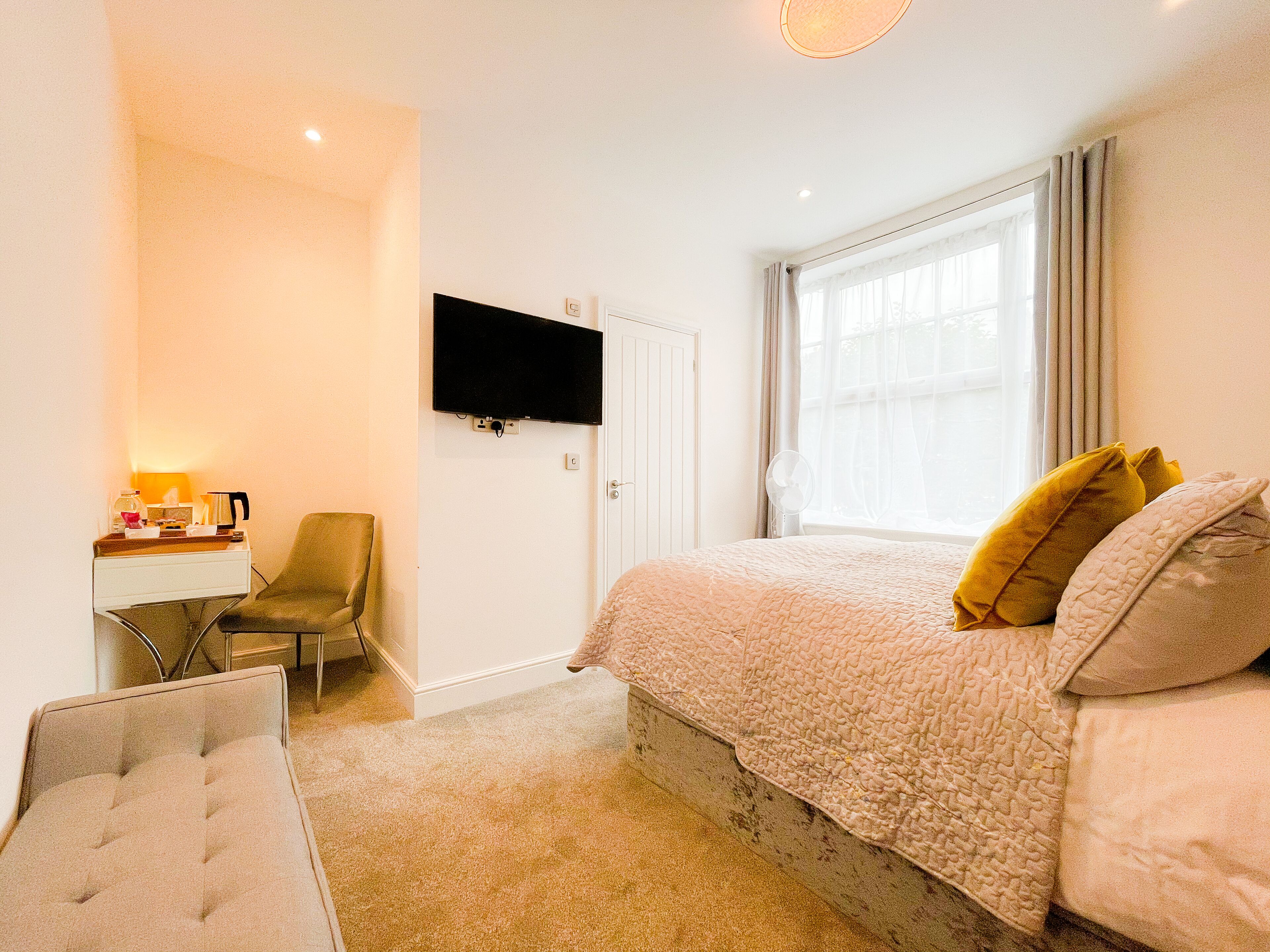 A bedroom with a bed, a desk, a chair, a TV, and a window.