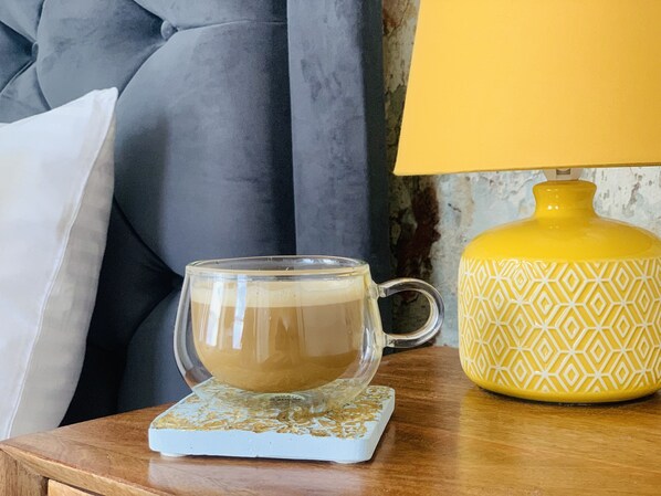 Una taza de vidrio transparente con un posavasos sobre una mesa de madera, junto a una lámpara amarilla con un diseño geométrico.