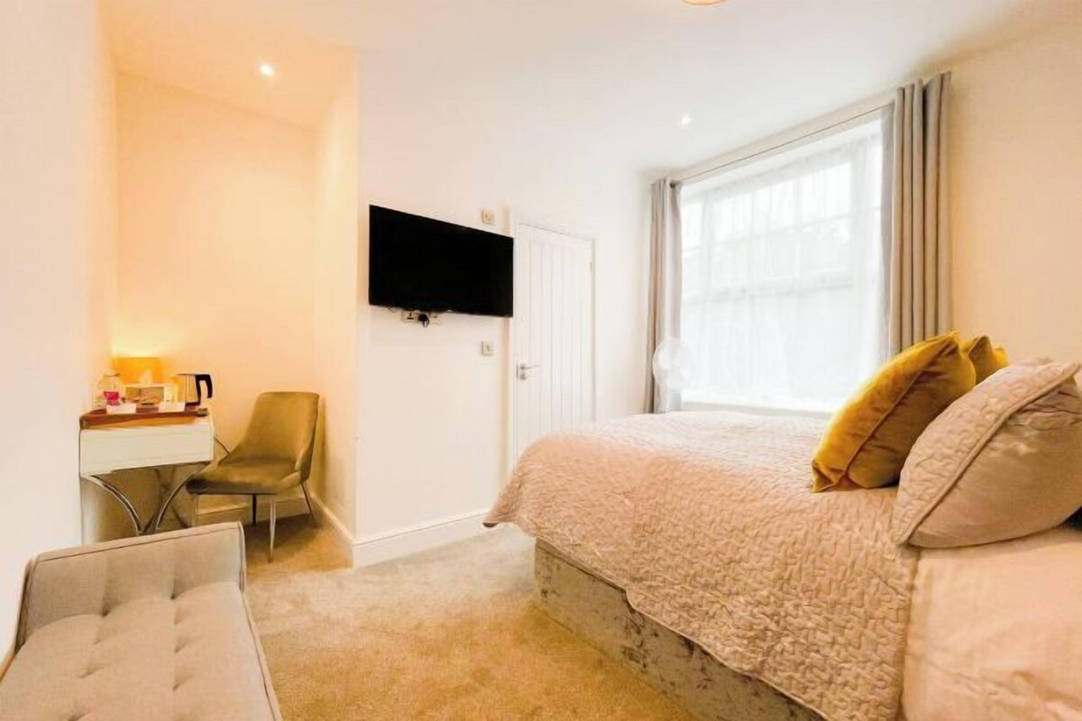 Una habitación de hotel con cama, escritorio, silla y televisión en la pared.