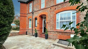 A red brick building with a stone patio, a small garden, and a sign for 'TW Services'. - Ashfield Boutique Stays (Altrincham)