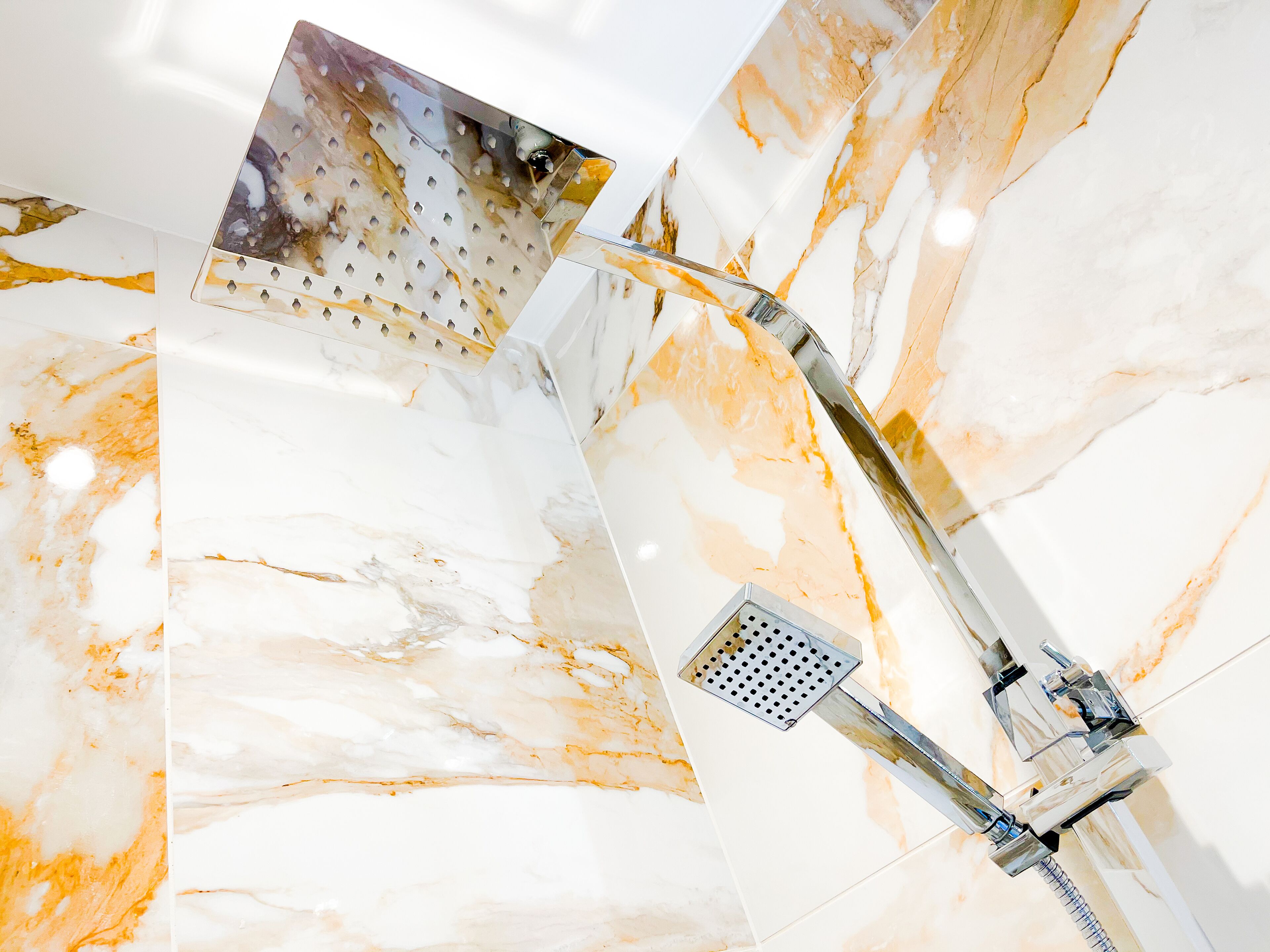 A modern bathroom with a marble wall, a shower with a transparent panel, and a chrome faucet.