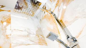 A modern bathroom with a marble wall, a shower with a transparent panel, and a chrome faucet.