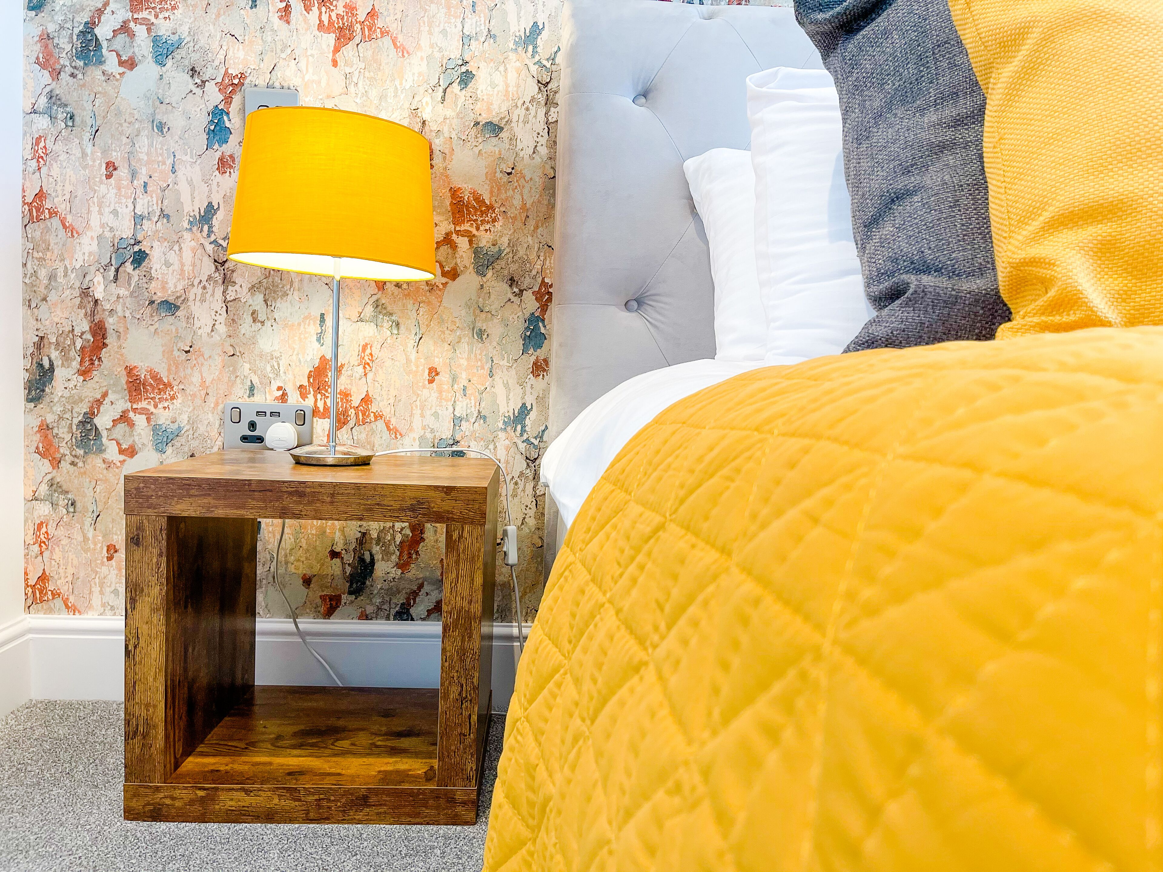 A bedroom with a bed, a nightstand with a lamp, and a wall with a textured pattern.